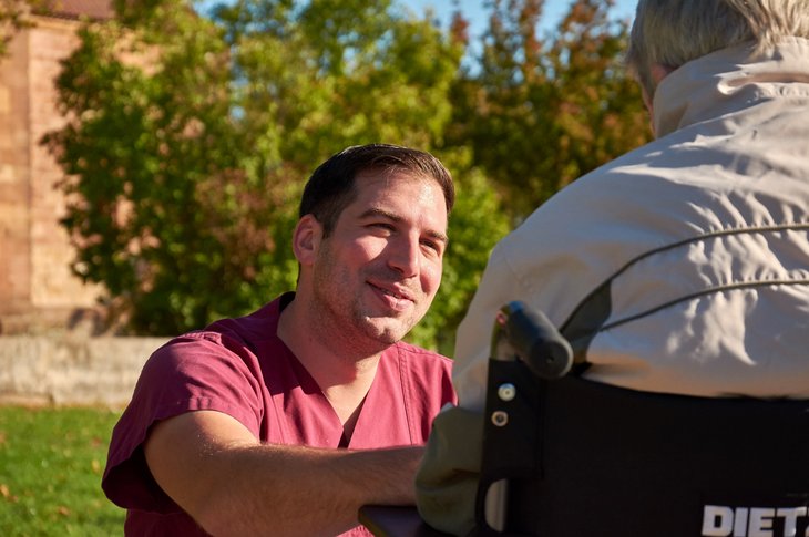 Ein Pflegefachmann kümmert sich um einen Patienten im Rollstuhl.
