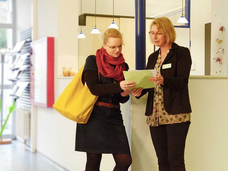 zwei Frauen stehen vor der Aufnahme und schauen auf einen Zettel welcher eine der Frauen in der Hand hält