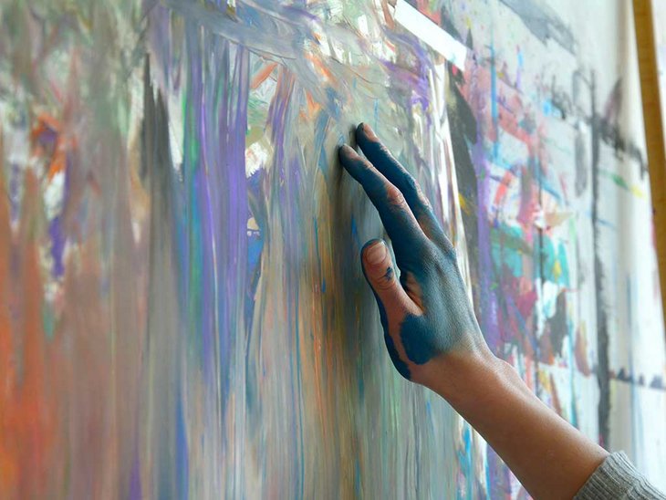 man sieht eine bunte Leinwand. Die Leinwand wird von einer Person mit den Händen bemalt.
