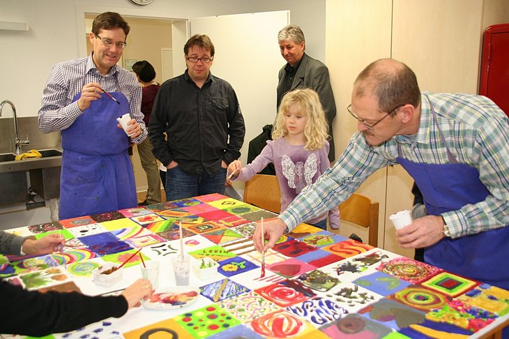 Am Eröffnungstag konnten die Besucher ein buntes Bild mitgestalten. Auch Pfalzklinikum-Geschäftsführer Paul Bomke (mit blauer Schürze links) und Dr. Markus Fani, Chefarzt der Klinik für Gerontopsychiatrie, (mit blauer Schürze rechts) malten mit.