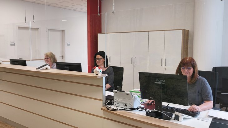 Empfangsbereich des MZEB Pfalzklinikum mit drei Mitarbeiterinnen, die an der Rezeption arbeiten